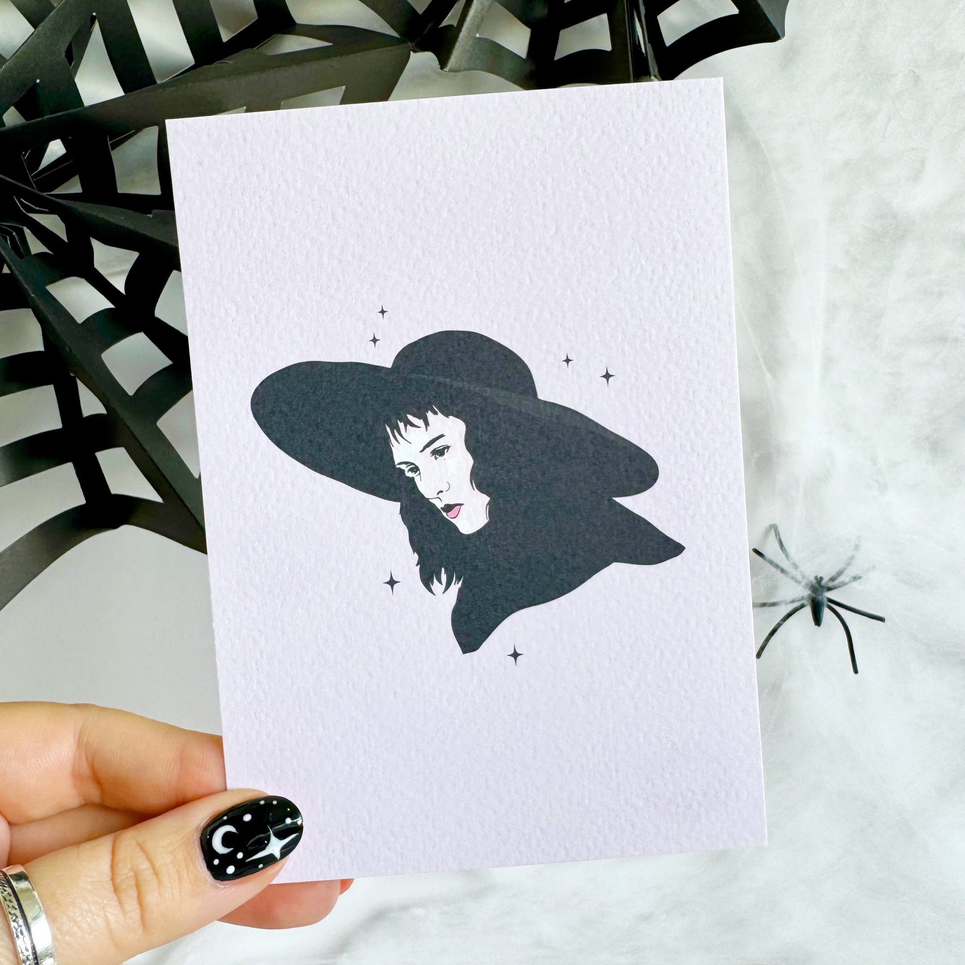 A halloween themed textured postcard with an illustration of Lydia Deetz, from Beetlejuice on the front.