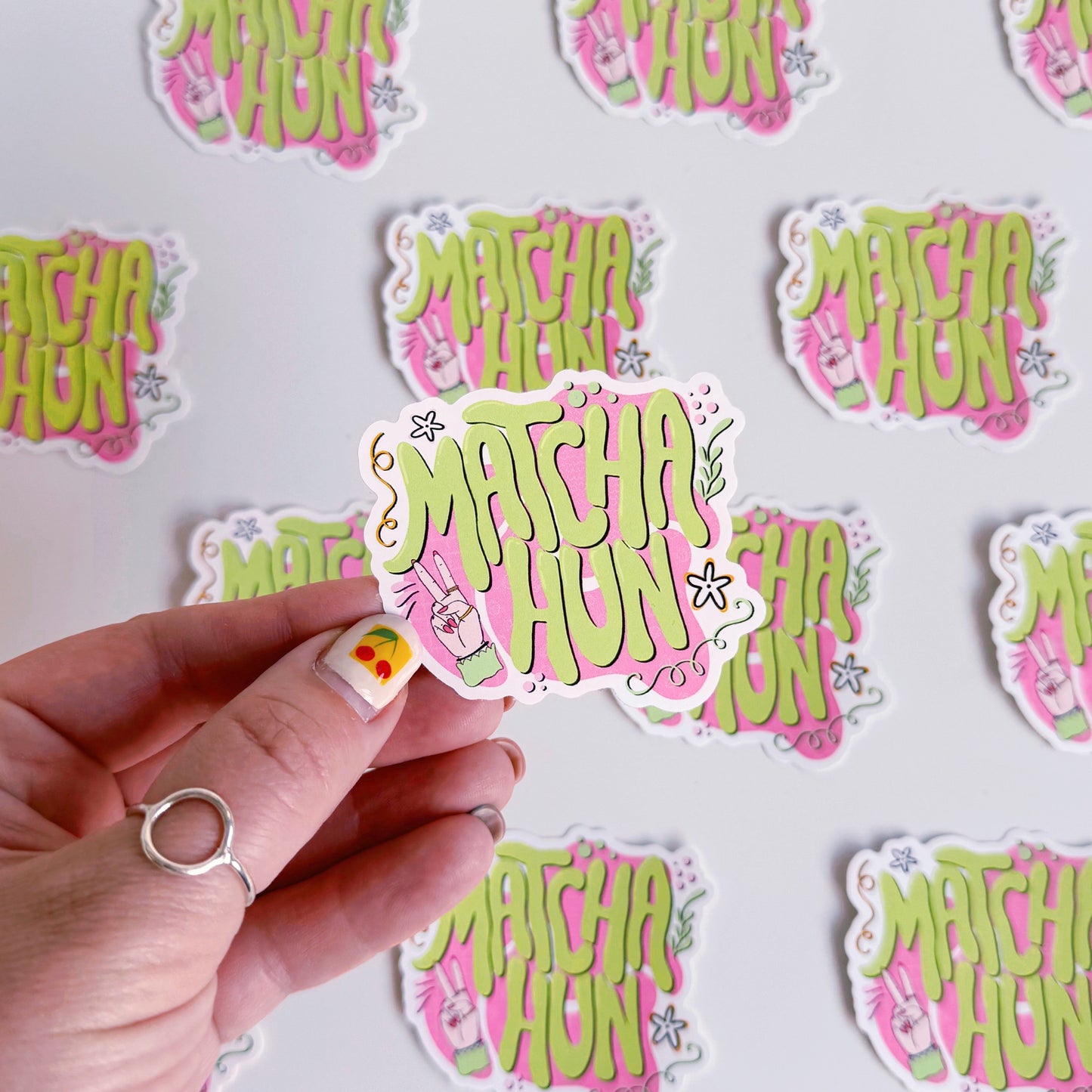 Several vinyl stickers on a white background. The vinyl sticker is pink and green and says the words 'Matcha Hun' in fun bubble writing. 