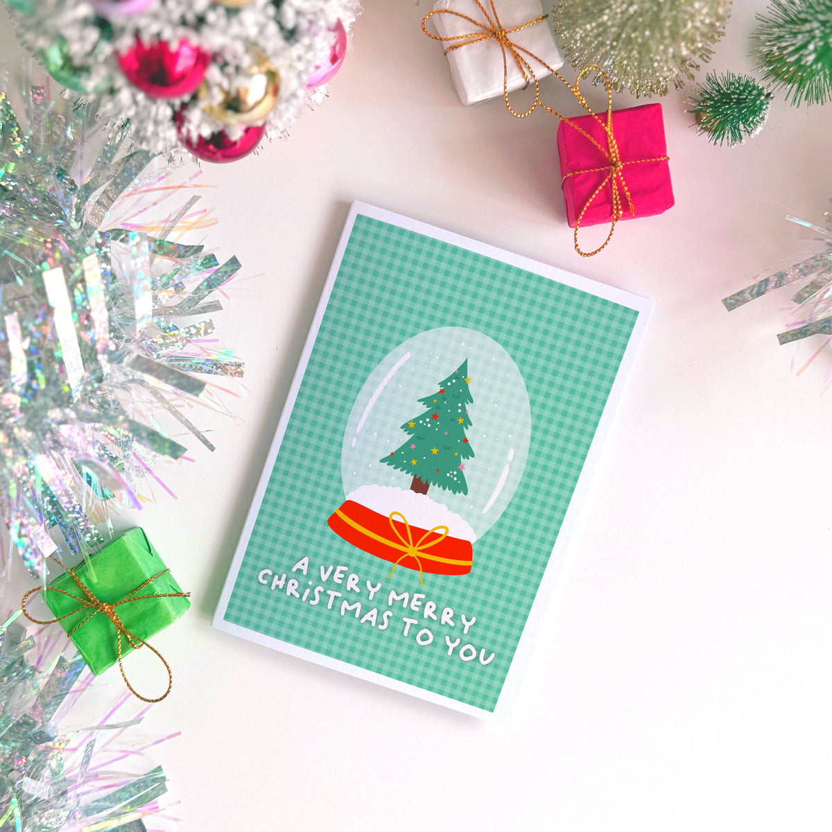 A green Christmas card with an illustration of a snow globe with a Christmas tree inside. The message on the front of the Christmas card reads 'A very Merry Christmas To you'