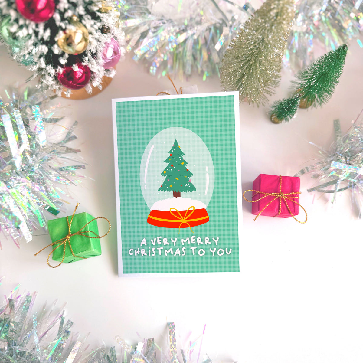 A green Christmas card with an illustration of a snow globe with a Christmas tree inside. The message on the front of the Christmas card reads 'A very Merry Christmas To you'