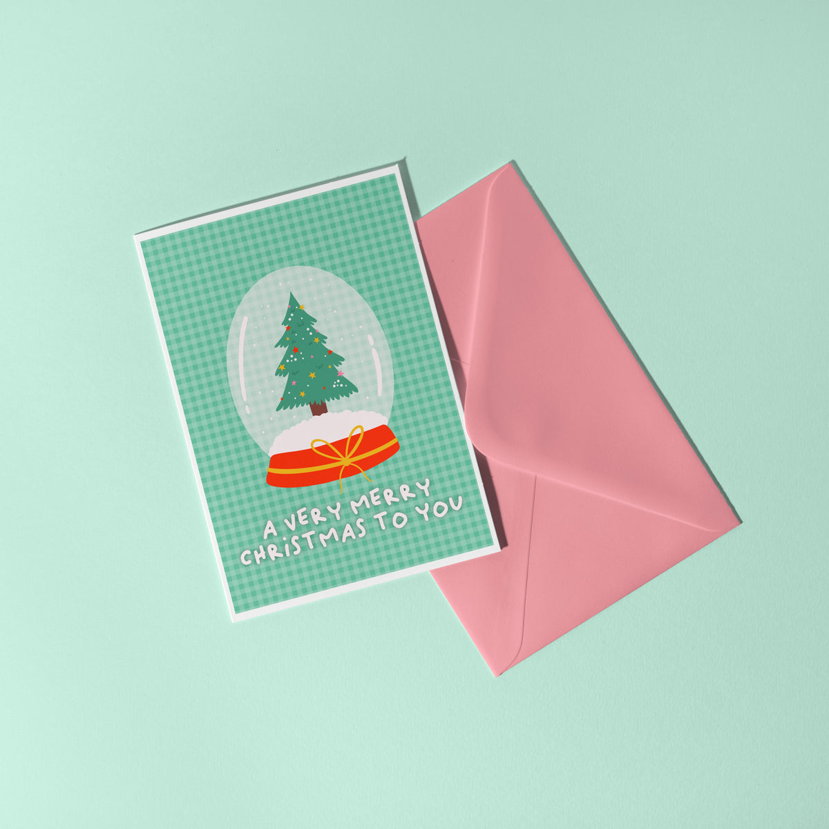 A green Christmas card with an illustration of a snow globe with a Christmas tree inside. The message on the front of the Christmas card reads 'A very Merry Christmas To you'