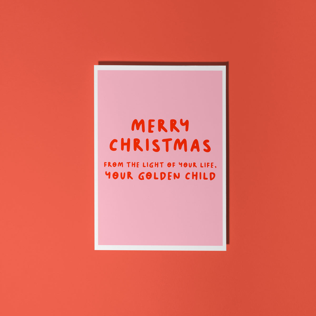A pink Christmas card with text in off-white that reads 'Merry Christmas from the light of your life, your golden child.'