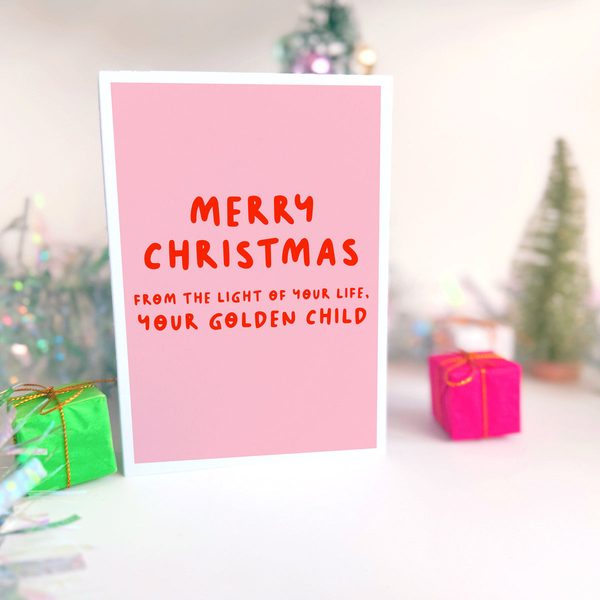 A pink Christmas card with text in off-white that reads 'Merry Christmas from the light of your life, your golden child.'