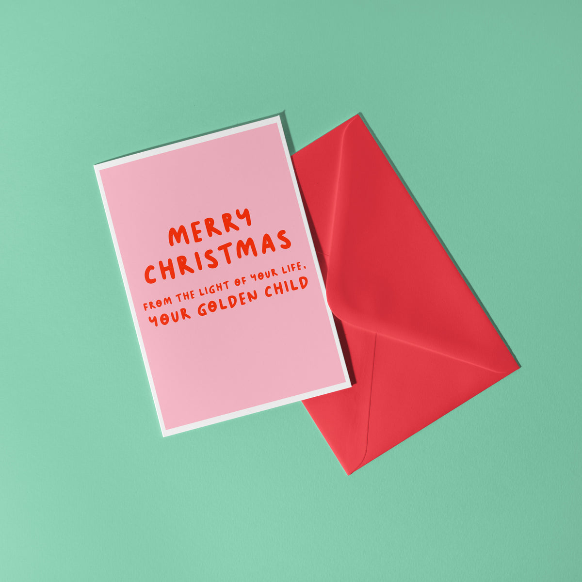 A pink Christmas card with text in off-white that reads 'Merry Christmas from the light of your life, your golden child.'