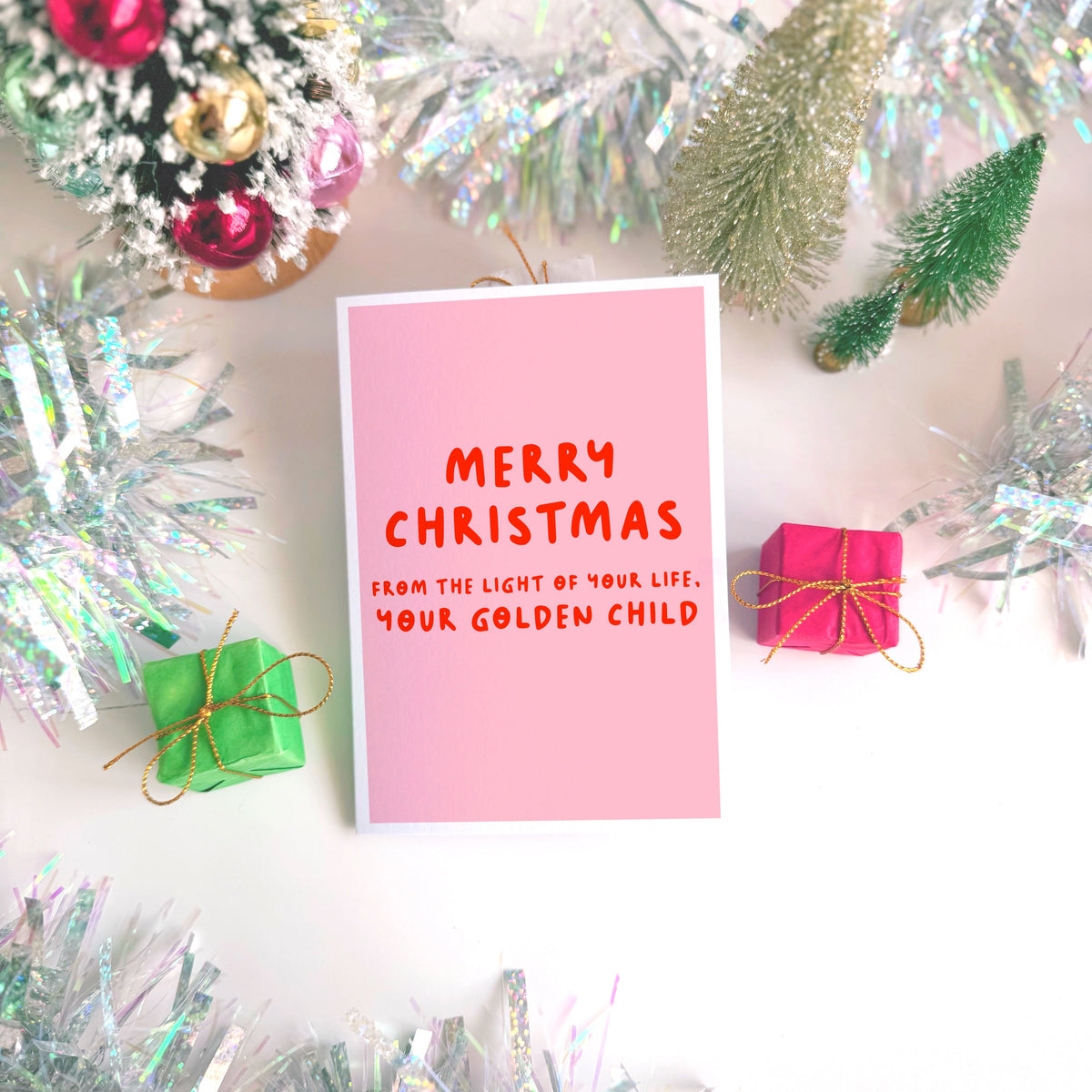 A pink Christmas card with text in off-white that reads 'Merry Christmas from the light of your life, your golden child.'
