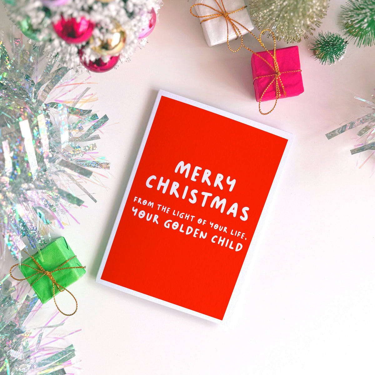 A red Christmas card with text in off-white that reads 'Merry Christmas from the light of your life, your golden child.'