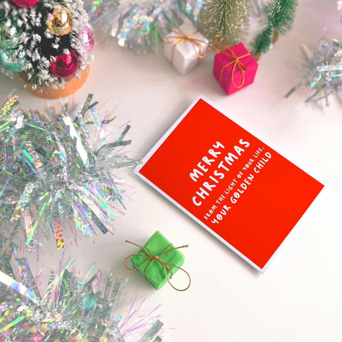 A red Christmas card with text in off-white that reads 'Merry Christmas from the light of your life, your golden child.'