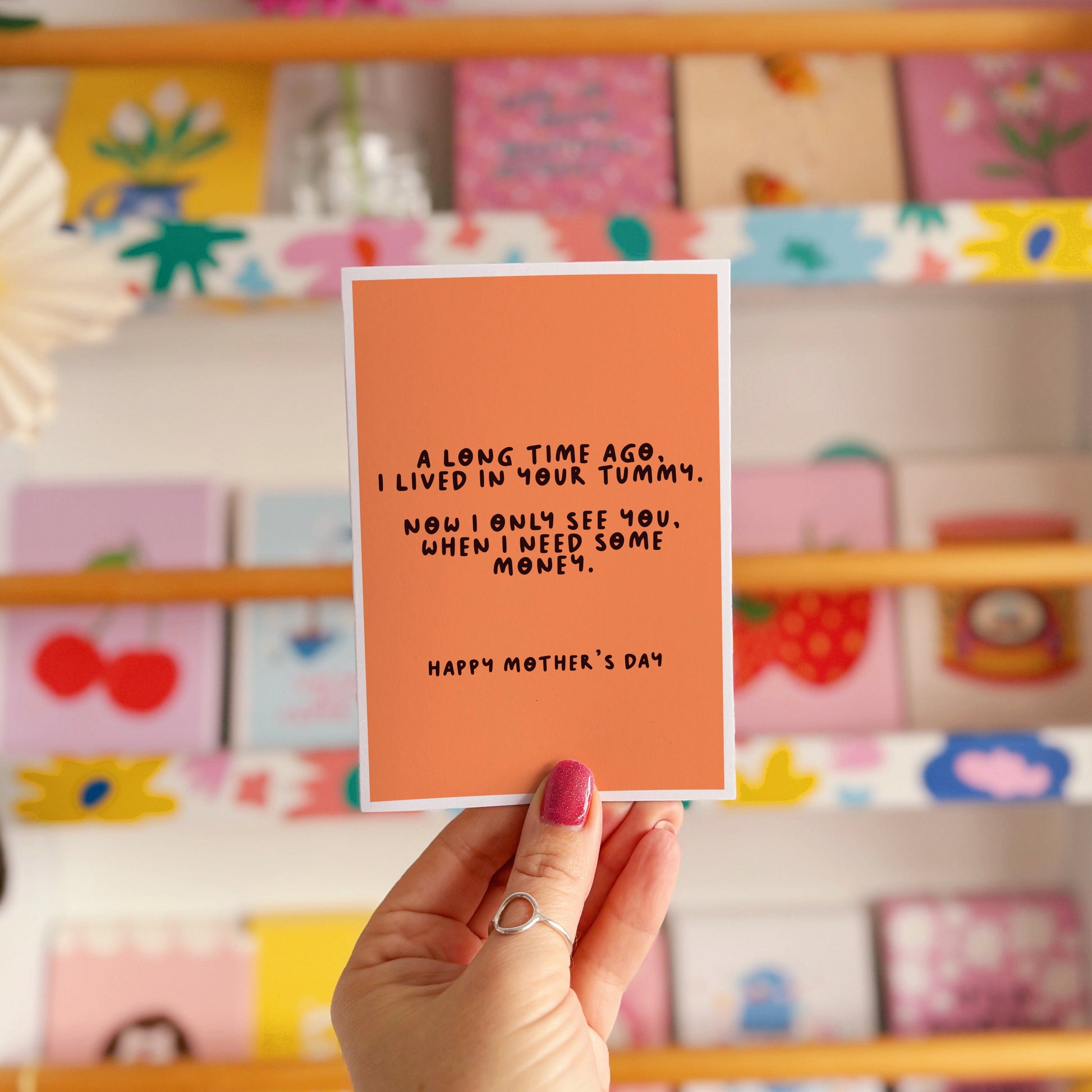 An orange Mother's Day card with a funny quote, that says 'A long time ago I lived in your tummy. Now I only see you, when I need some money. Happy Mother's Day".