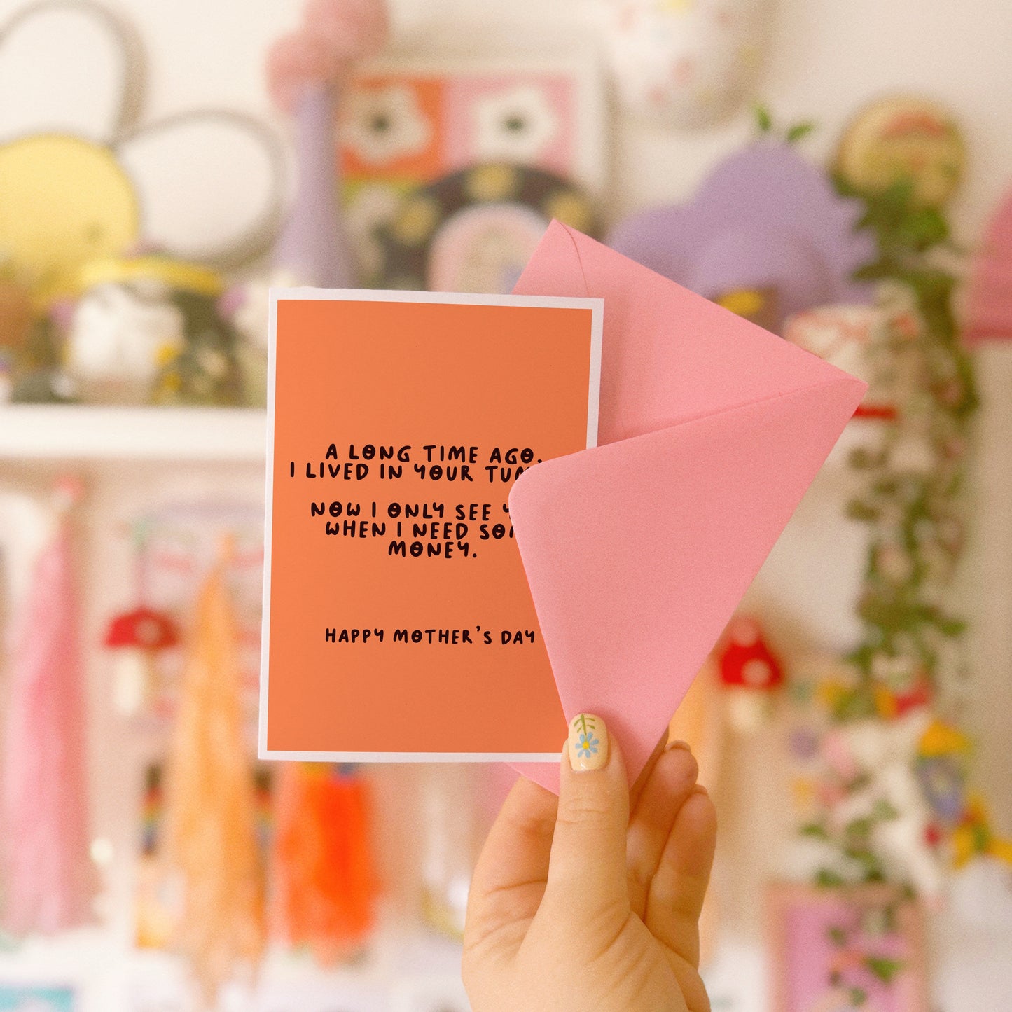 An orange Mother's Day card with a funny quote, that says 'A long time ago I lived in your tummy. Now I only see you, when I need some money. Happy Mother's Day".