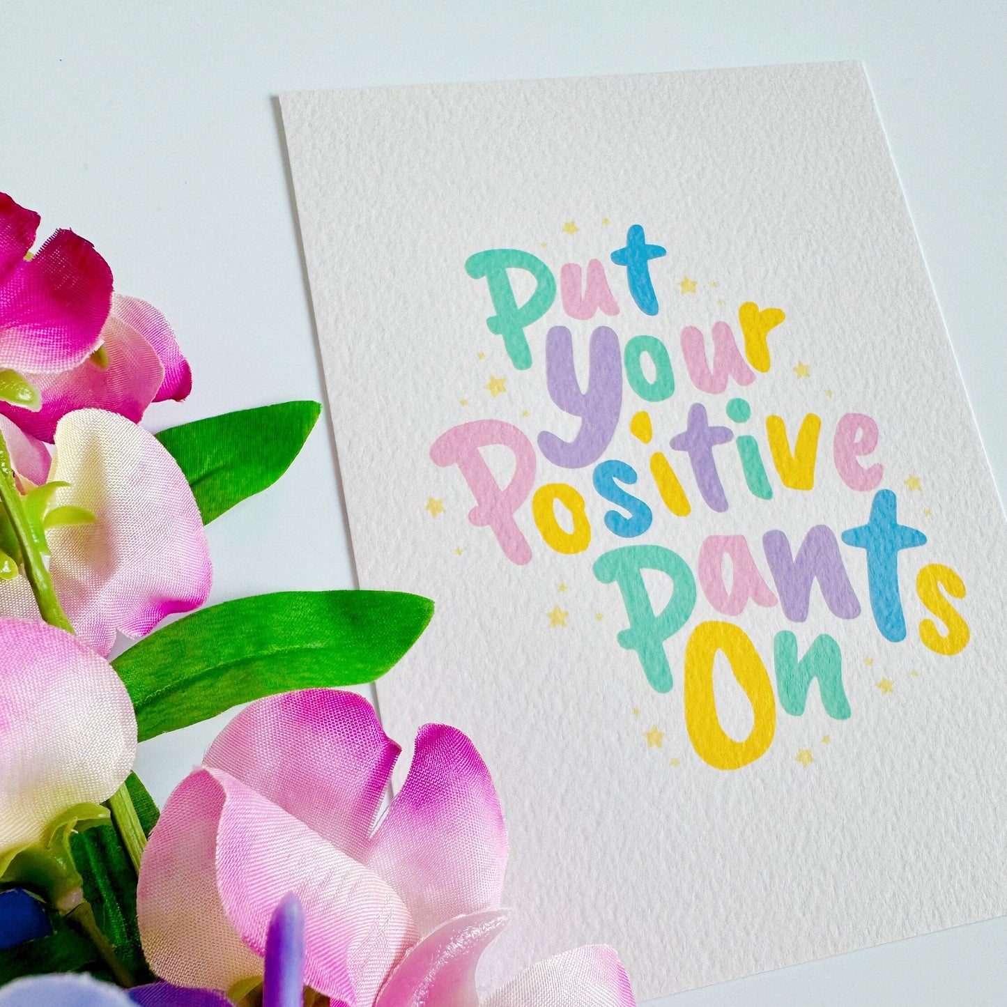 A textured postcard, with the words put your positive pants on, on the front, in pastel colours.