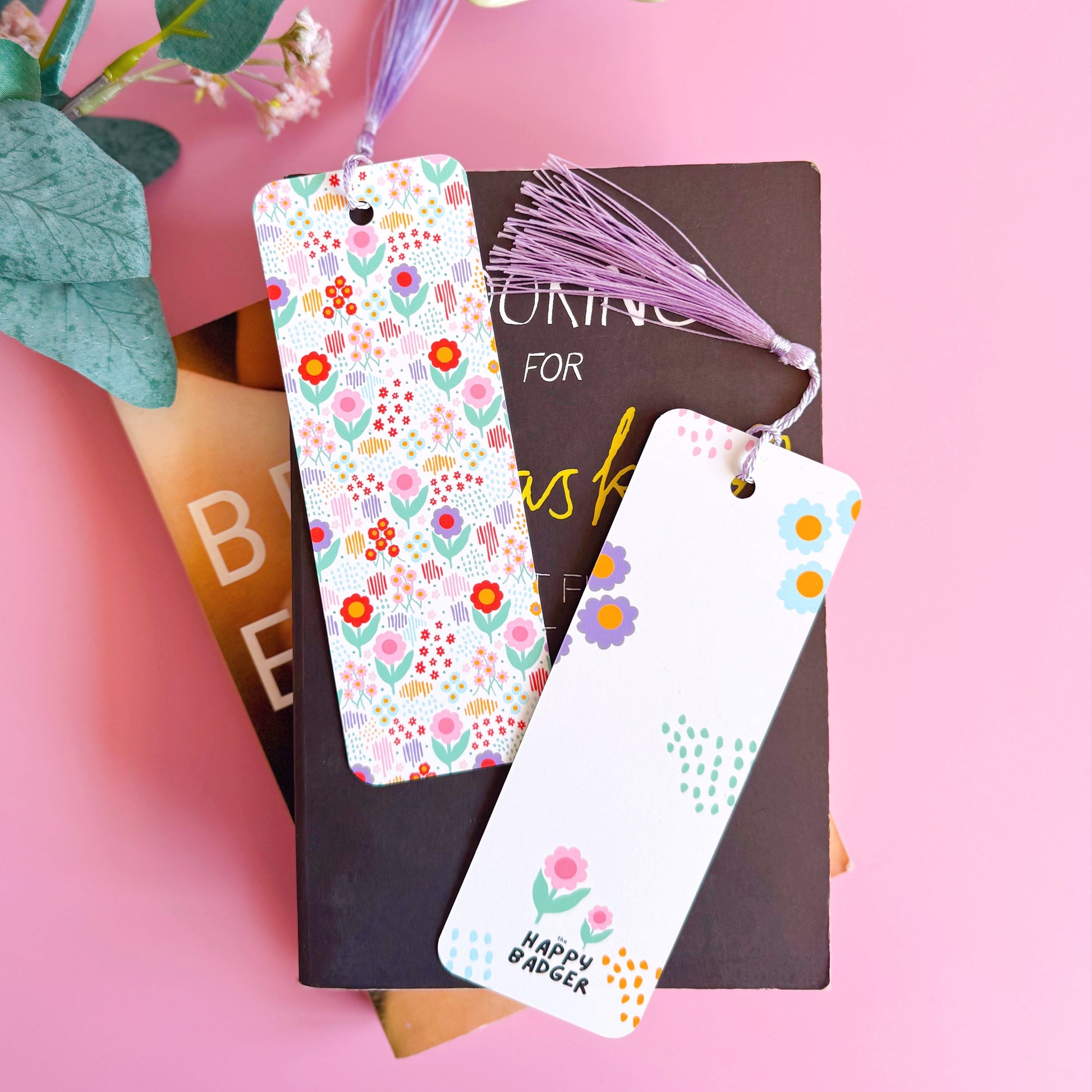 A multi coloured floral bookmark, with a coordinating lilac purple tassel. The pattern is on a white background and features pink, green, purple and red across the flower pattern.