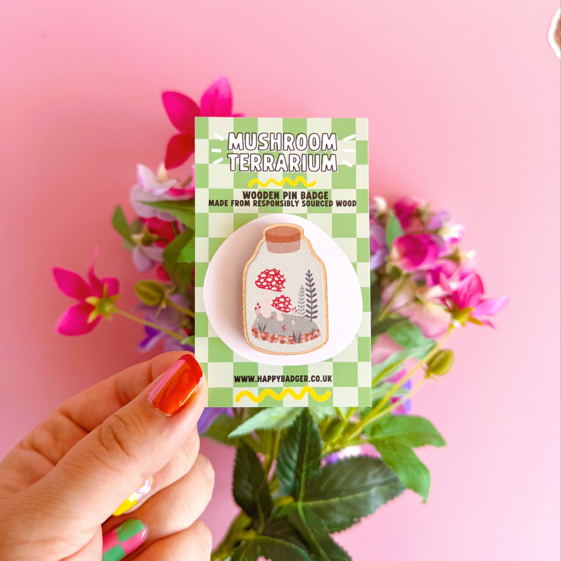 A wooden pin badge featuring an illustration of a terrarium filled with mushrooms and woodland elements.