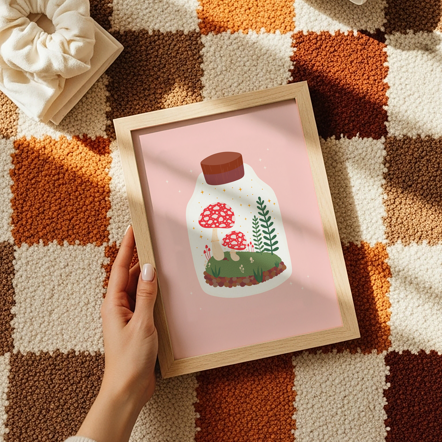 An illustration of a terrarium jar with toadstools and greenery inside of it. The background of the illustration print is a soft warm pink.