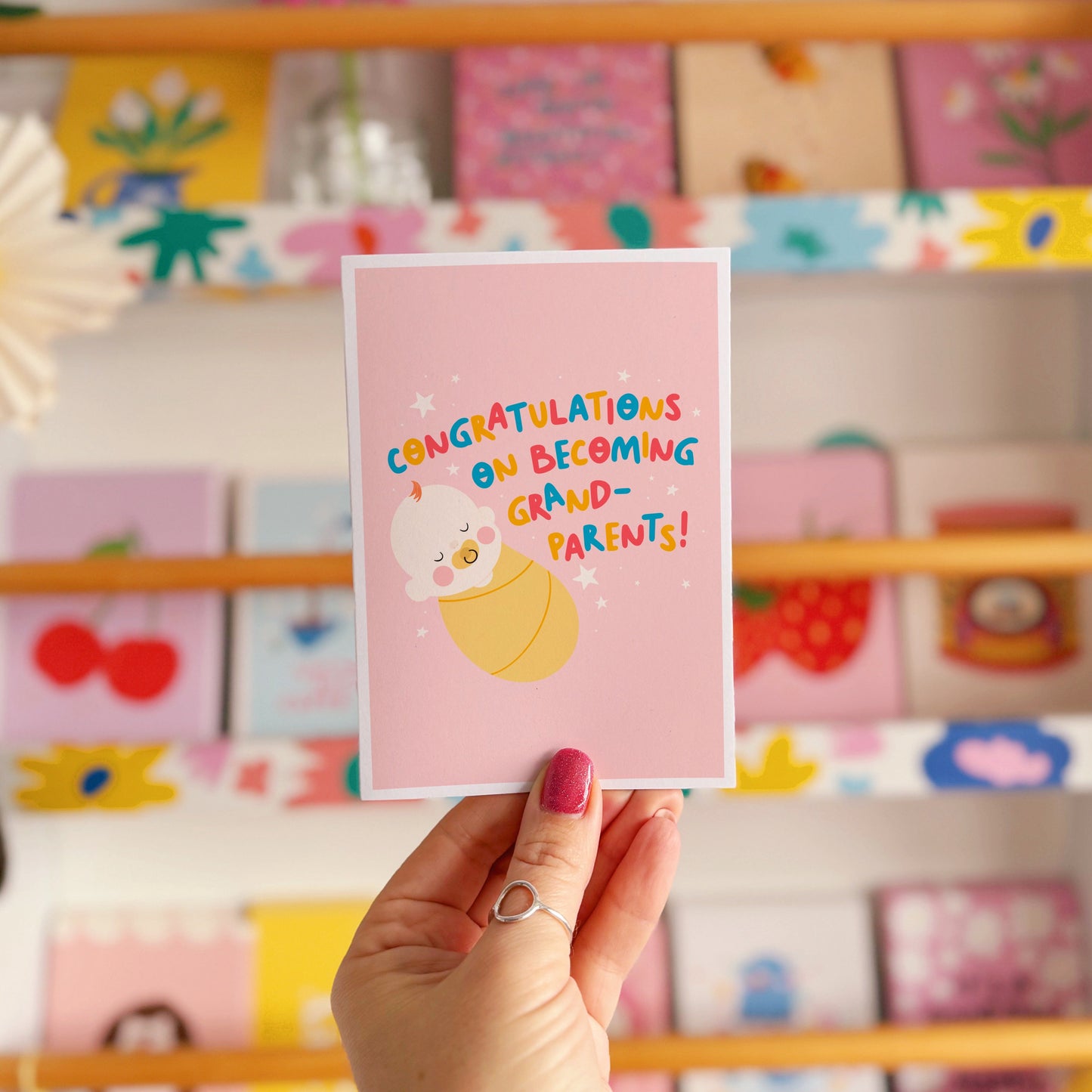 A card for congratulating new grandparents on the arrival of their new grandchild, with an illustration of a baby and colourful text.