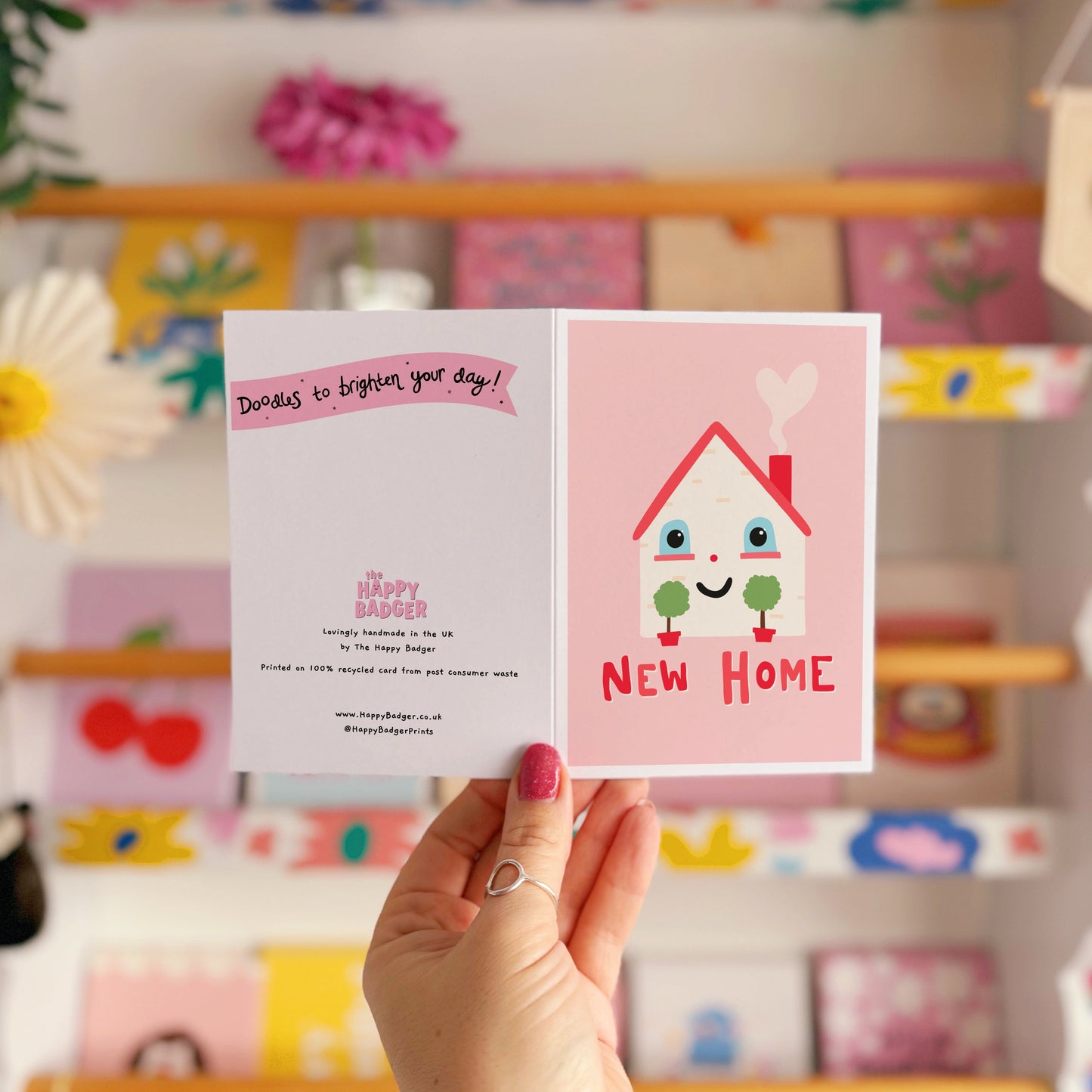 A new home congratulations card with an illustration of a little house with a smiling face and hand lettering underneath that reads 'New Home'.