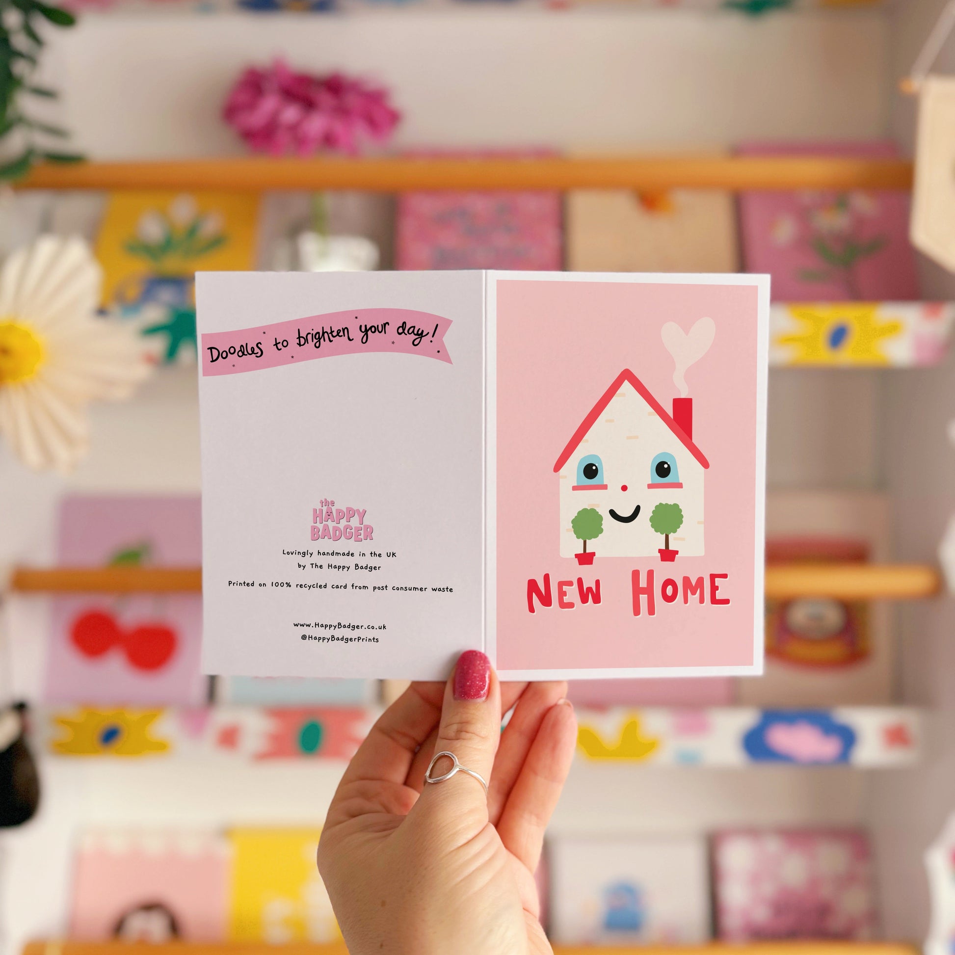 A new home congratulations card with an illustration of a little house with a smiling face and hand lettering underneath that reads 'New Home'.