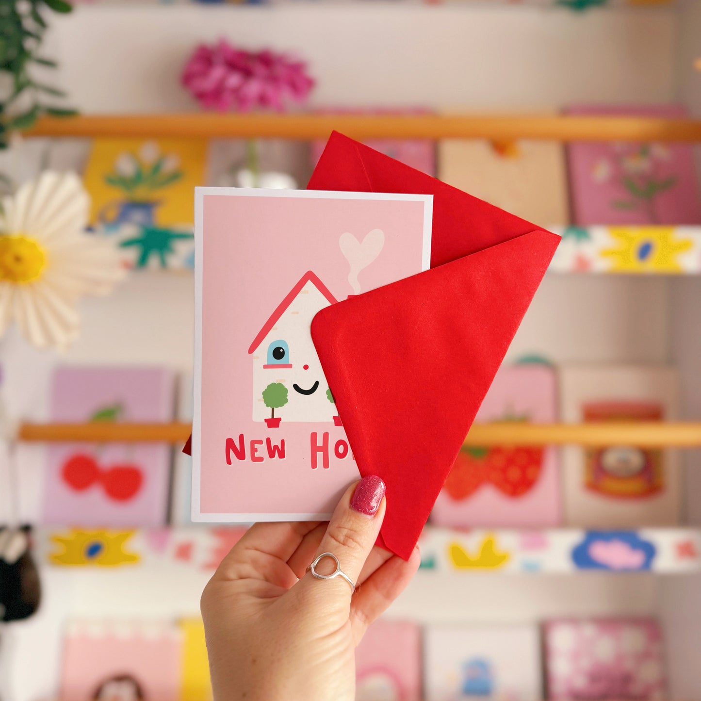 A new home congratulations card with an illustration of a little house with a smiling face and hand lettering underneath that reads 'New Home'.