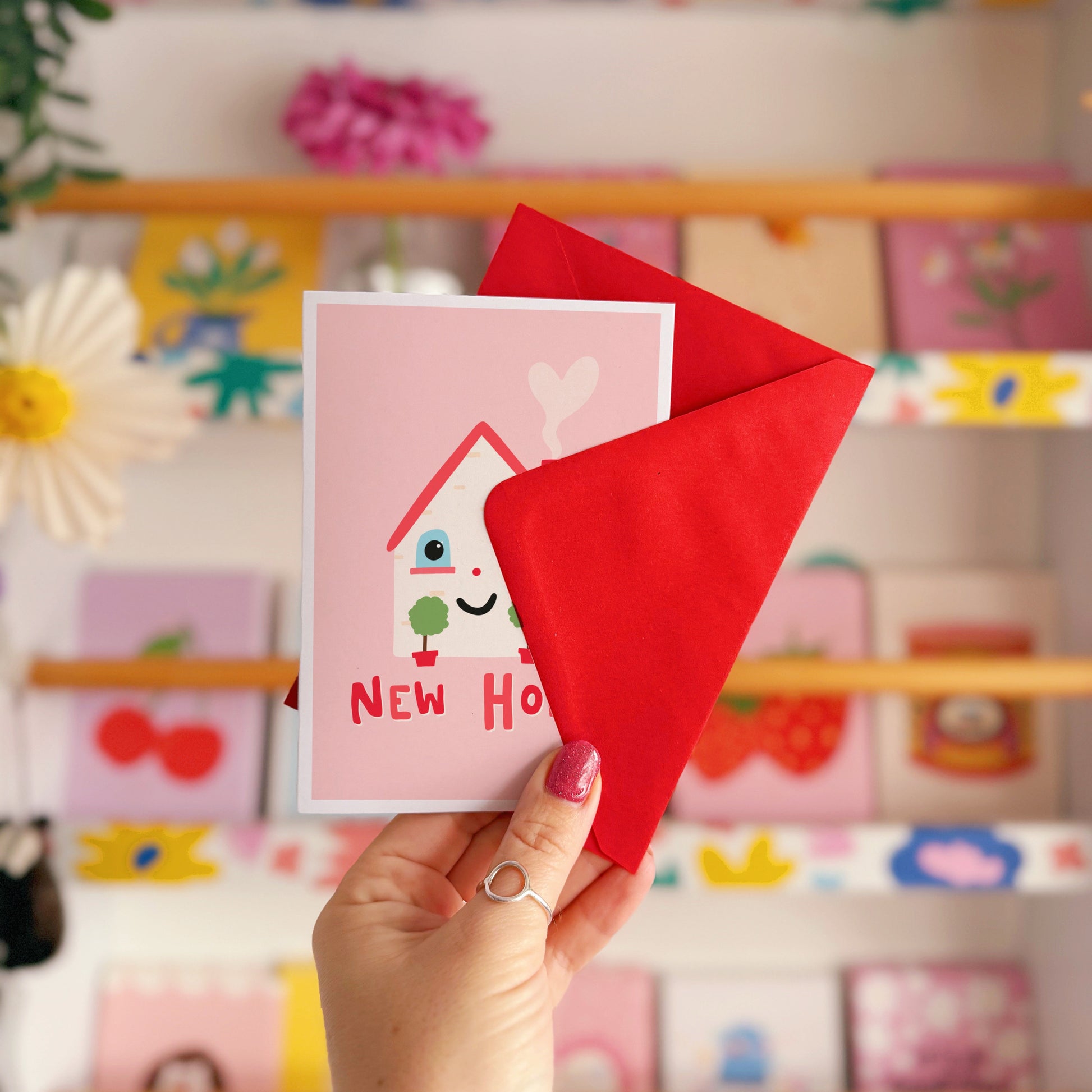 A new home congratulations card with an illustration of a little house with a smiling face and hand lettering underneath that reads 'New Home'.