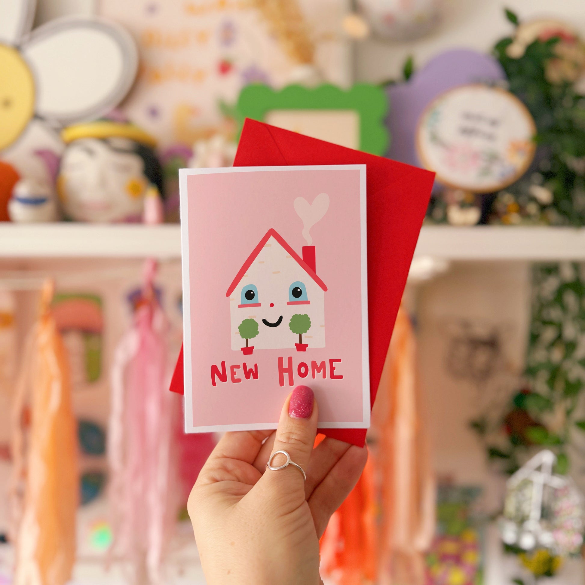 A new home congratulations card with an illustration of a little house with a smiling face and hand lettering underneath that reads 'New Home'.