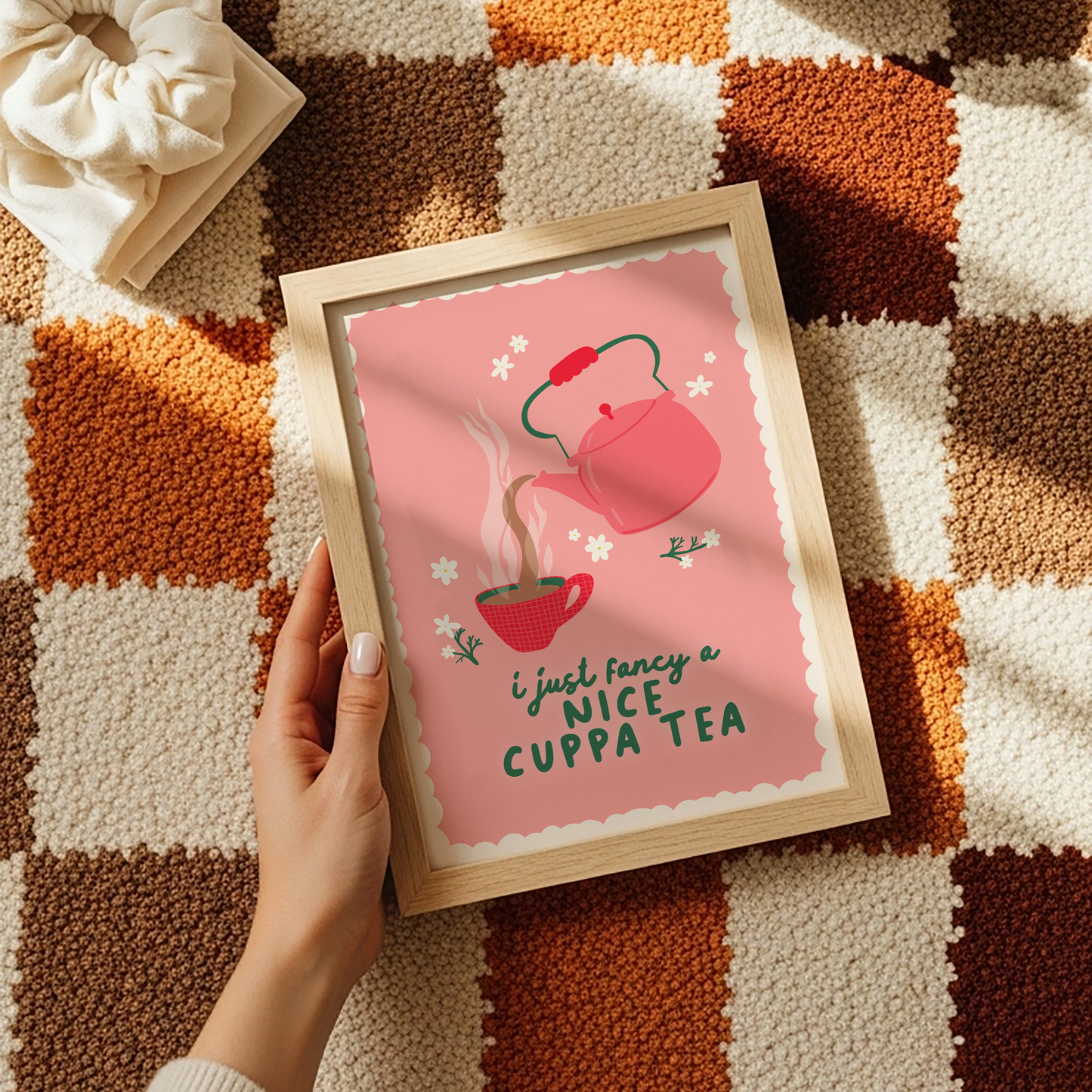 A pink print with a scalloped edge border, with a teapot and mug illustration and a cosy quote.