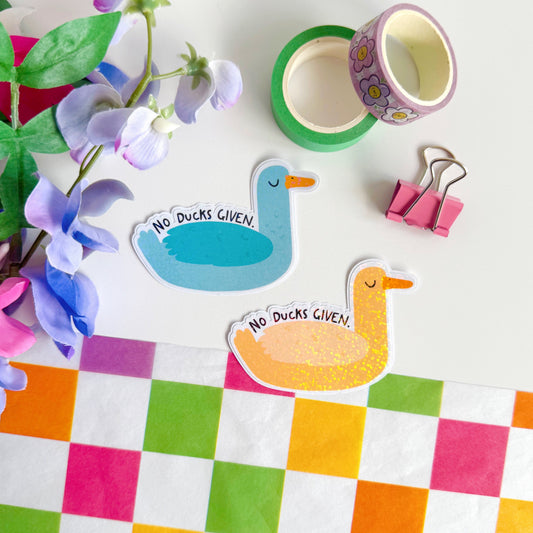 Two cute and funny duck stickers, one blue and one yellow, with the words 'no ducks given' above their wings. They have a glittery effect to the stickers.