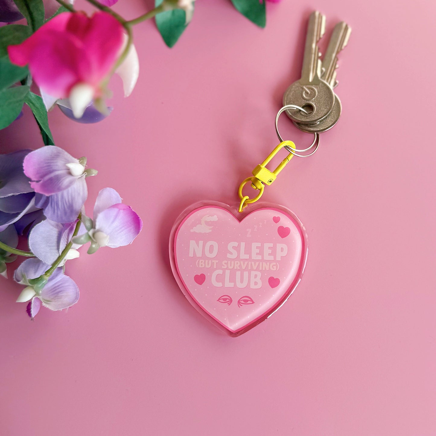 Heart-shaped keychain with 'No Sleep But Surviving Club' on, with a yellow clasp.