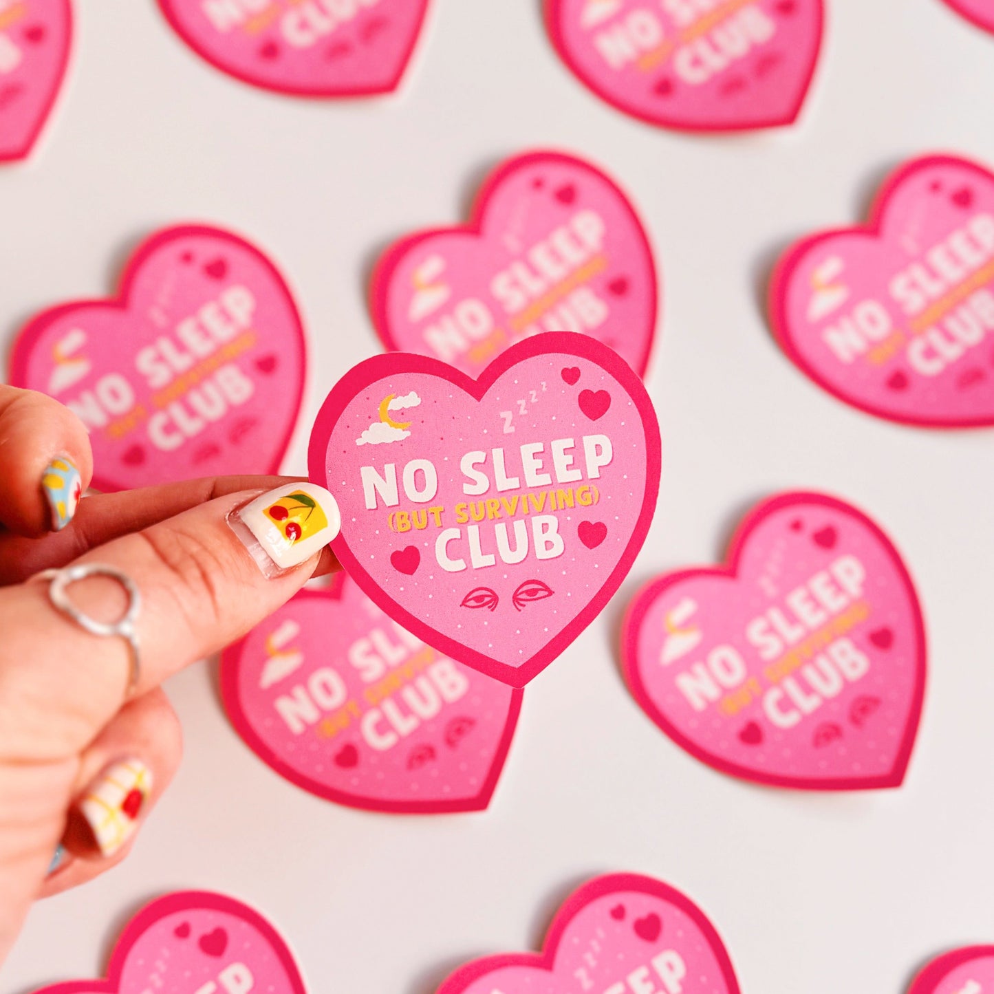 A pink heart-shaped sticker with a 'No Sleep Club' quote and little illustrations relating to sleep and tiredness.