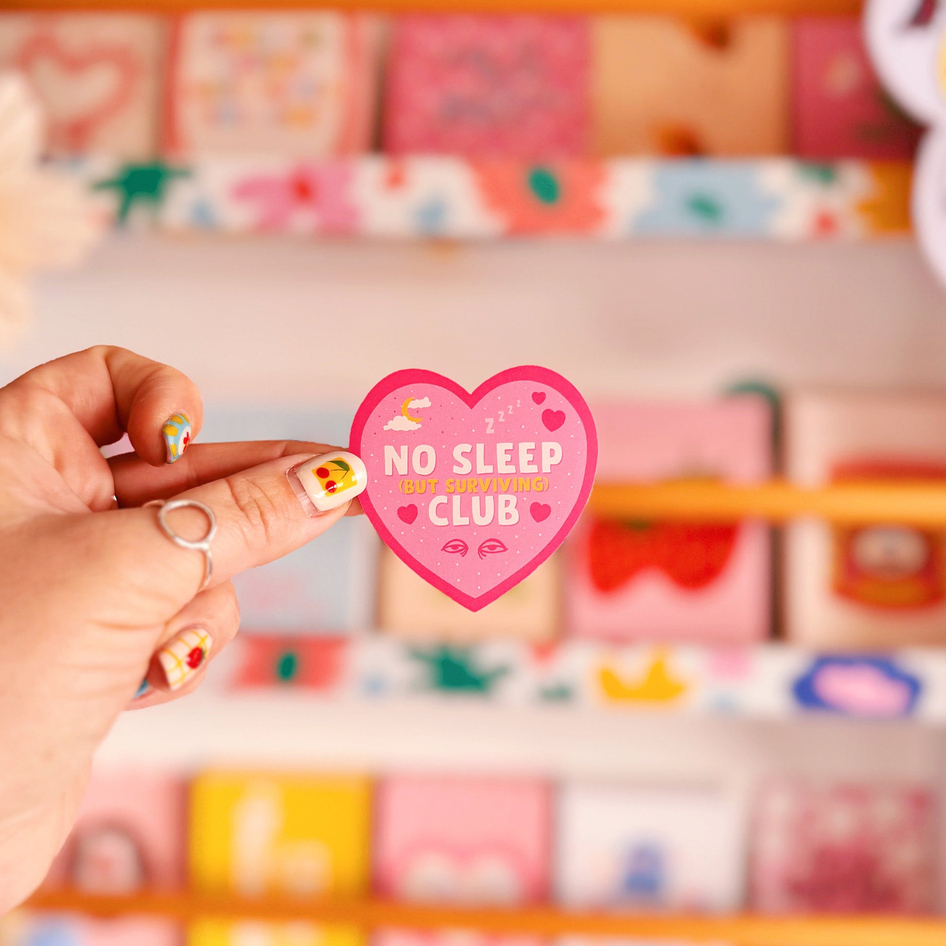 A pink heart-shaped sticker with a 'No Sleep Club' quote and little illustrations relating to sleep and tiredness.