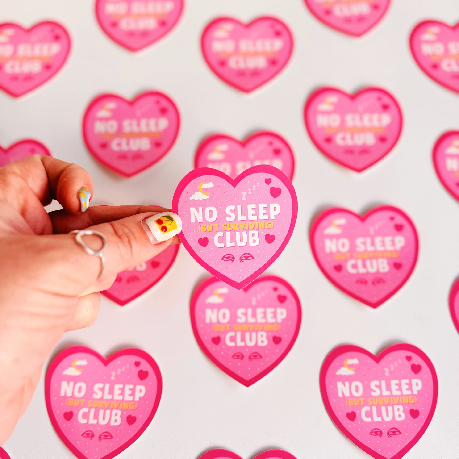 A pink heart-shaped sticker with a 'No Sleep Club' quote and little illustrations relating to sleep and tiredness.