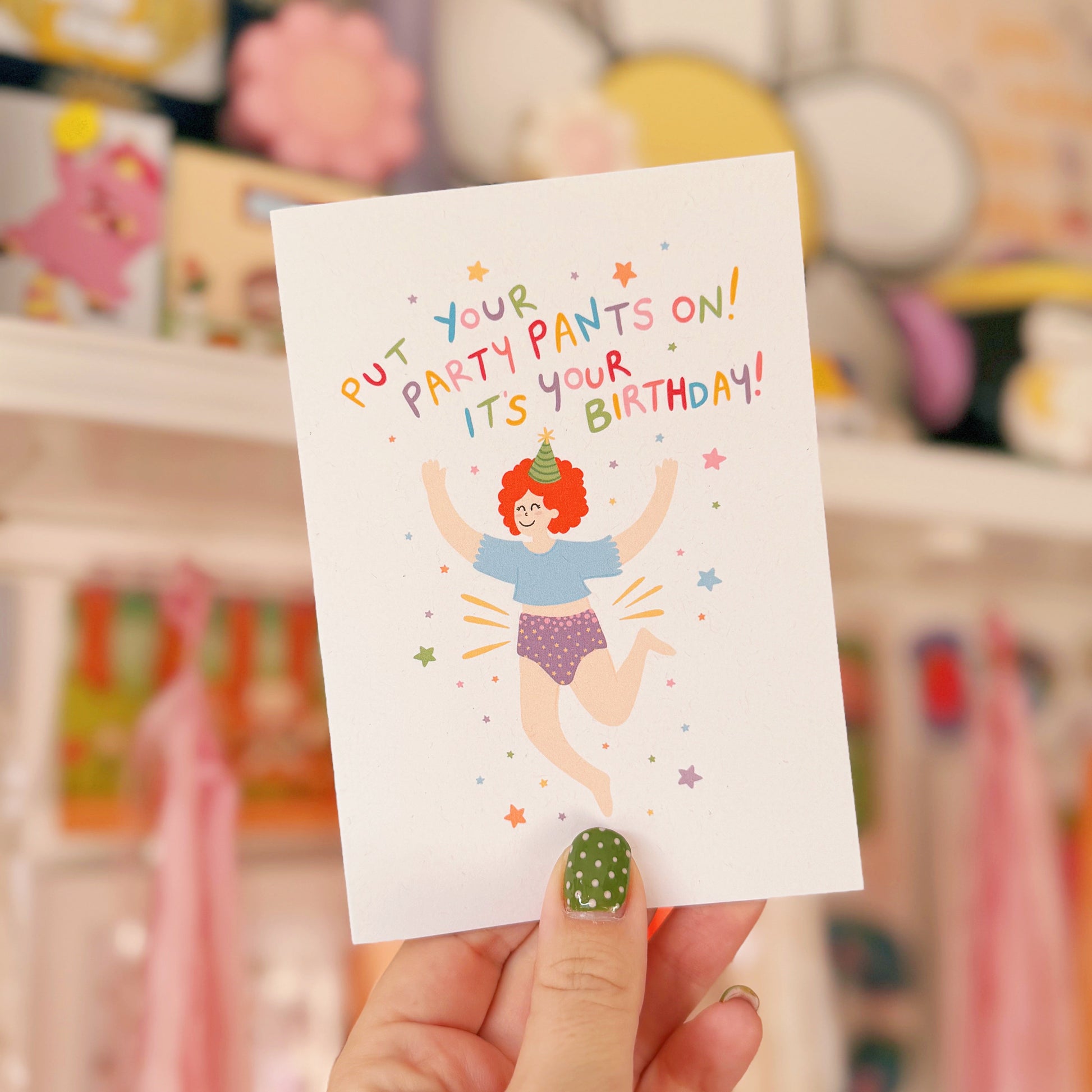 Hand holding a birthday card with colourful text and illustration in a festive setting.