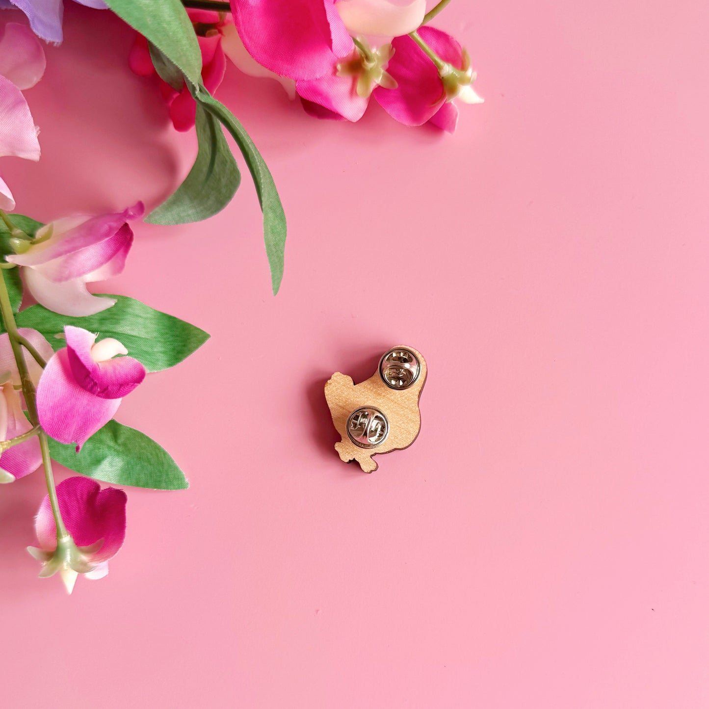 The back of a wooden pin badge with two metal clasp fastenings.