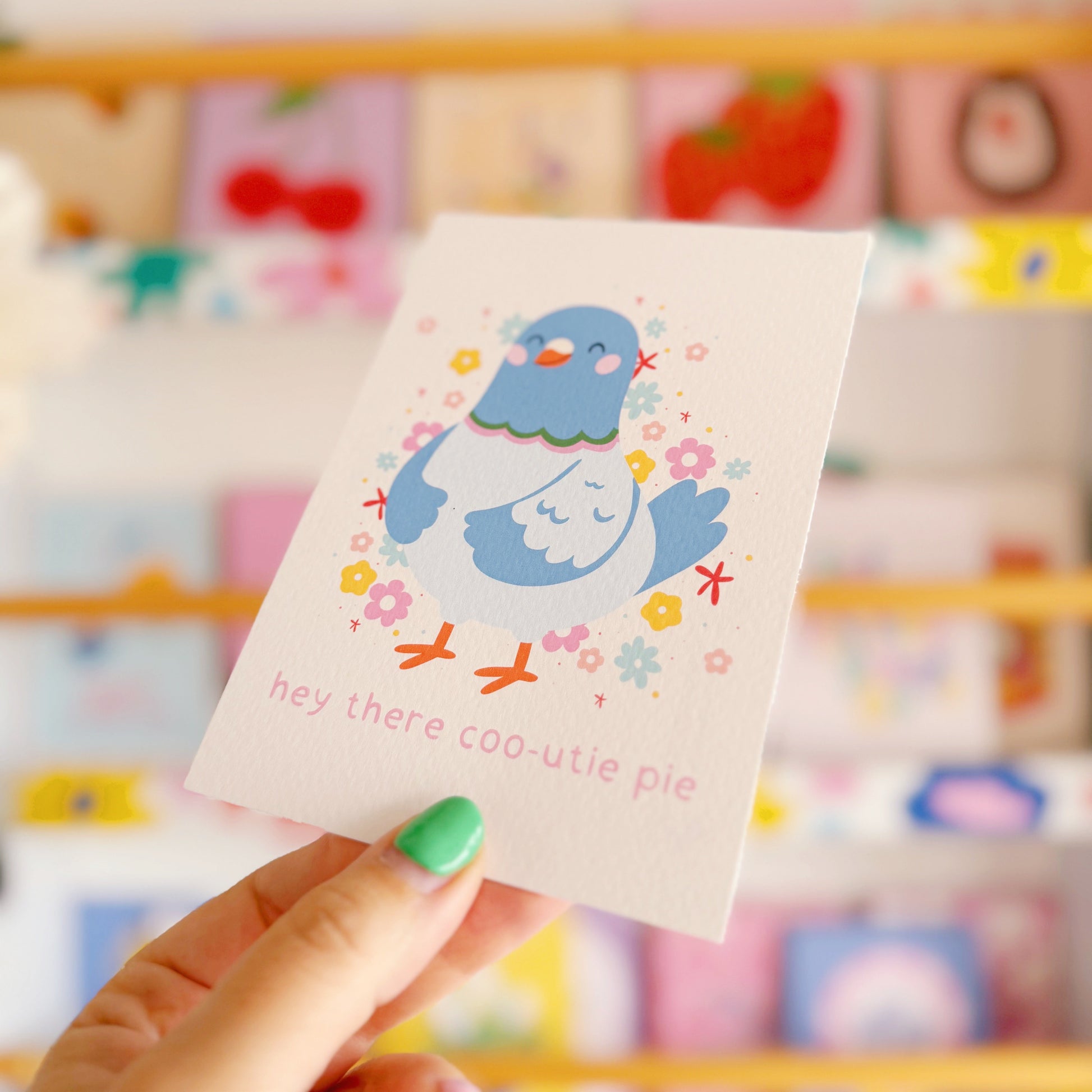 Card with a cartoon pigeon held by a hand against a colourful background