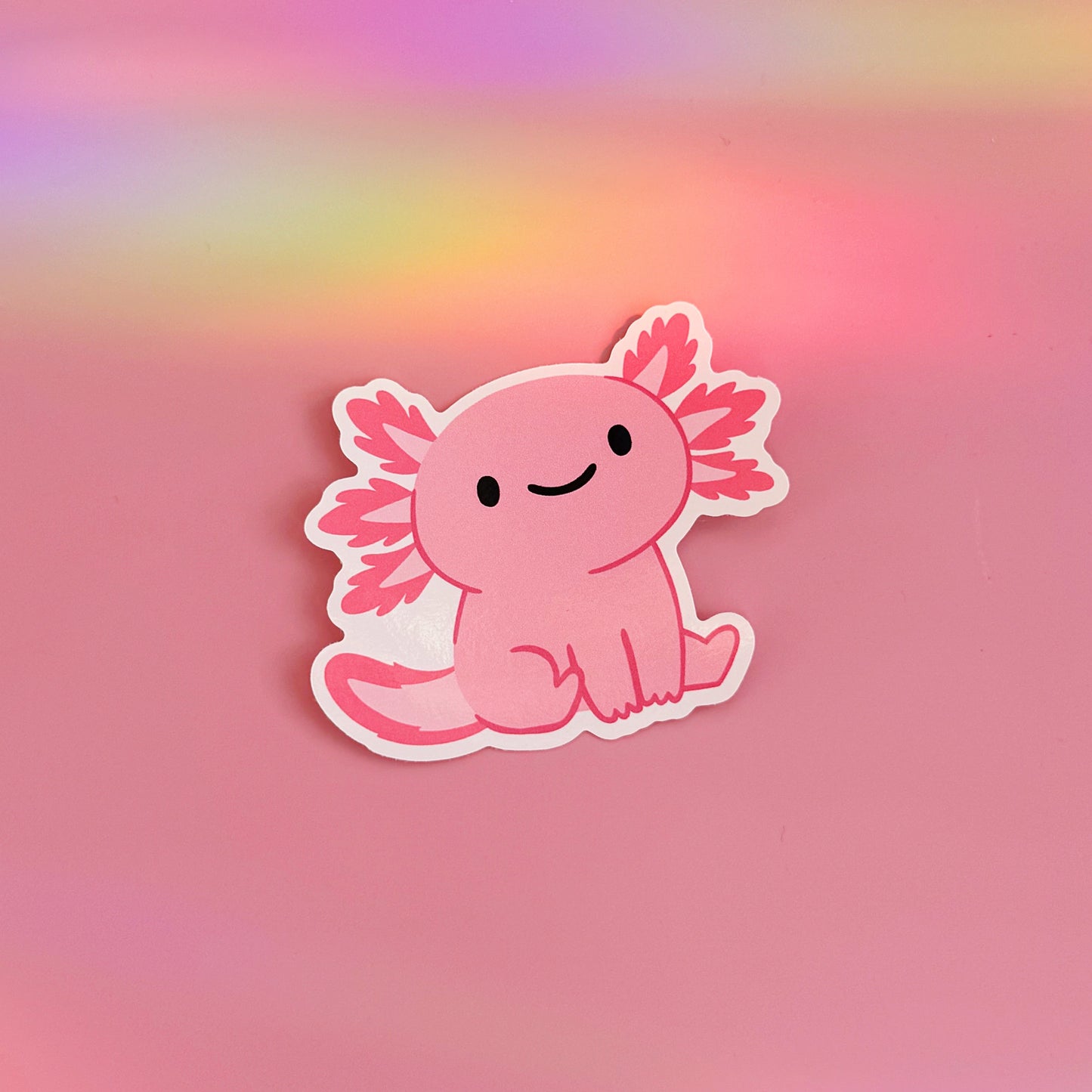 A waterproof vinyl sticker featuring an illustration of a cute pink smiling axolotl. 