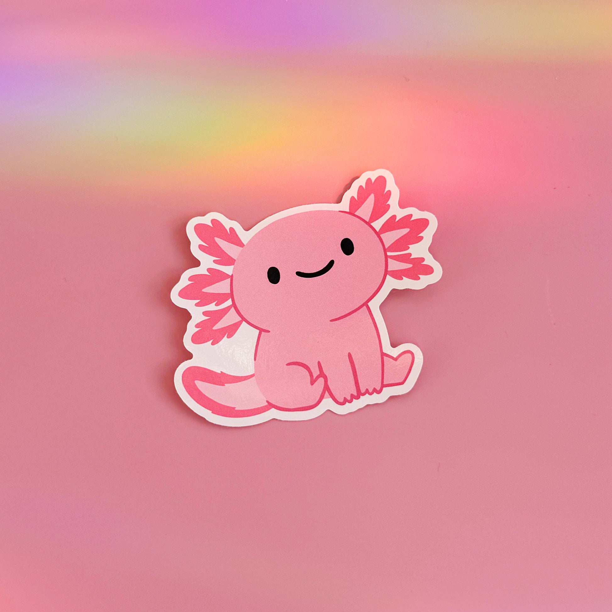 A waterproof vinyl sticker featuring an illustration of a cute pink smiling axolotl. 