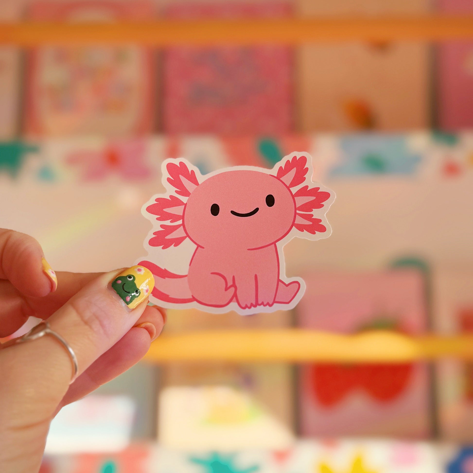 A waterproof vinyl sticker featuring an illustration of a cute pink smiling axolotl. 