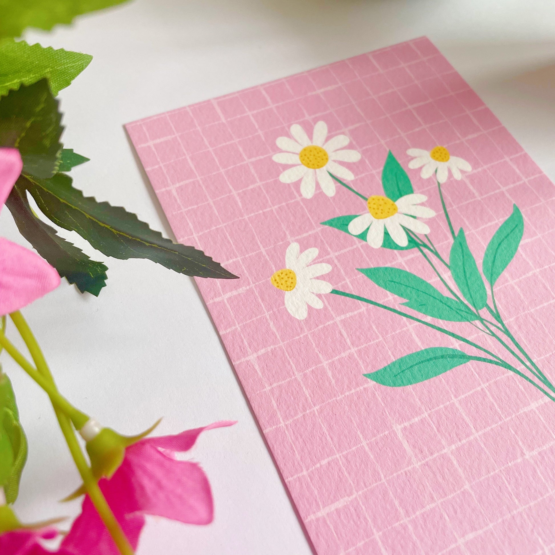 A pink textured postcard with an illustration of four daisies with bright green stems.