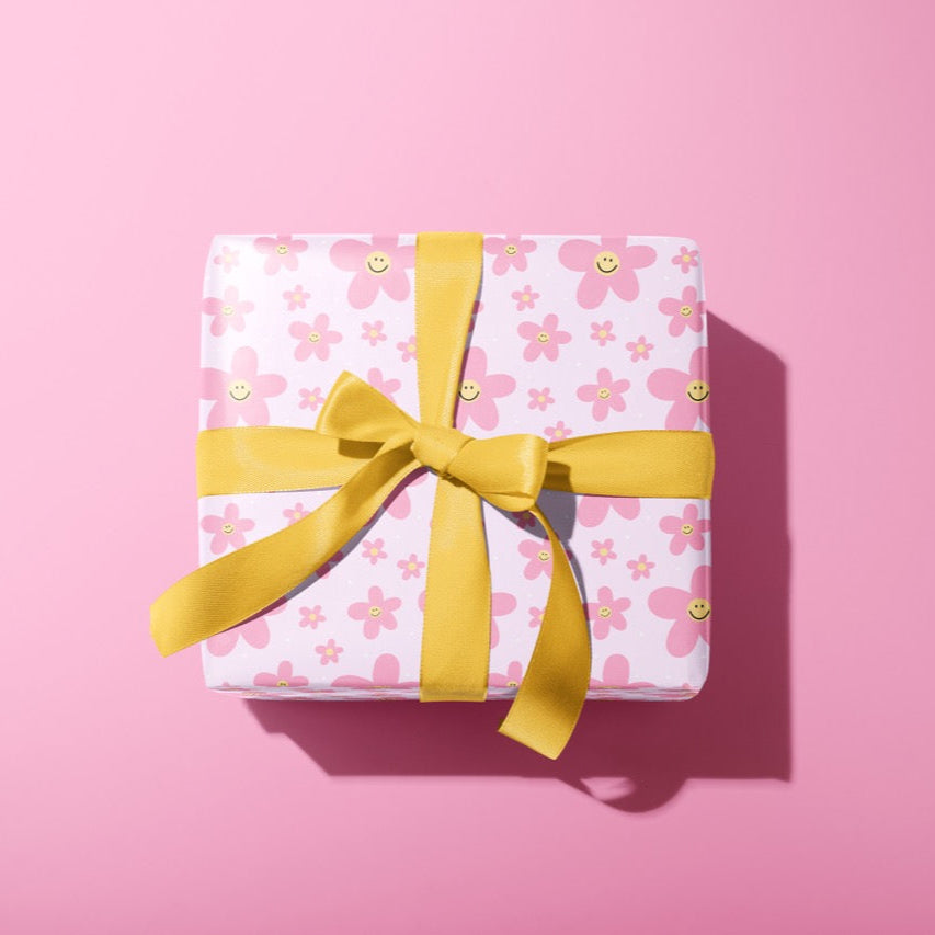 A present wrapped in pink wrapping paper with pink smiling daisies all over it. Tied up with a yellow ribbon.