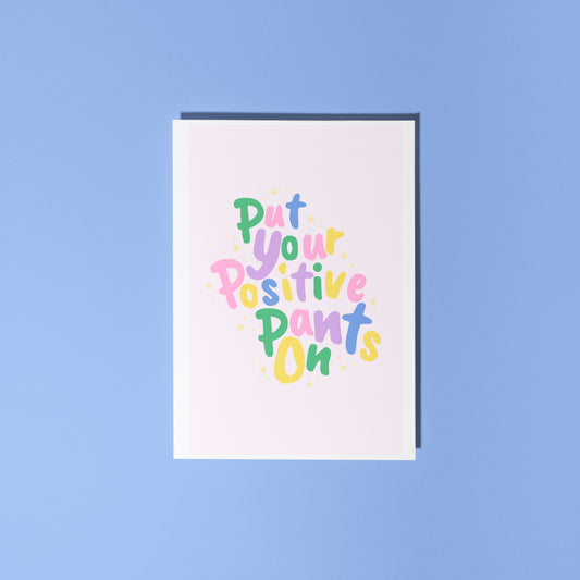 A colourful card with hand lettered text, saying 'put your positive pants on' on a light pink background.