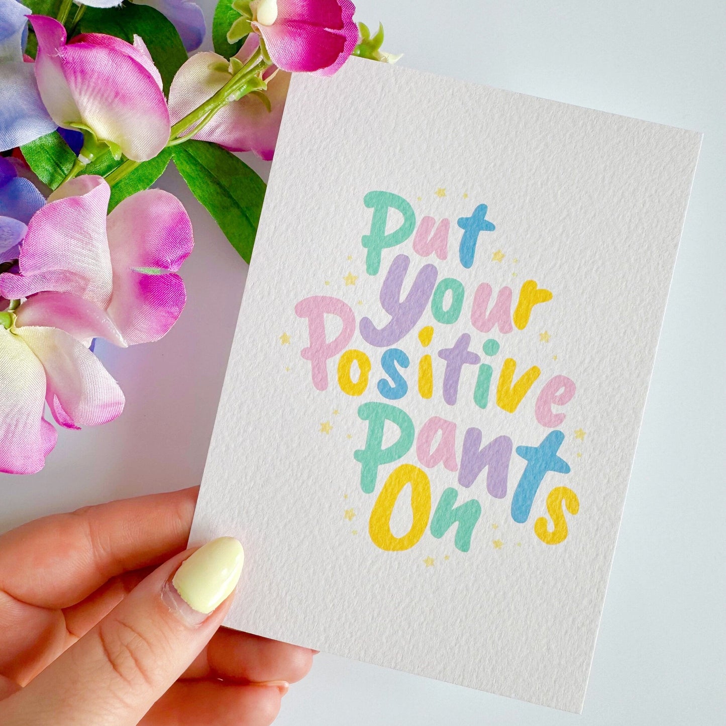 A textured postcard, with the words put your positive pants on, on the front, in pastel colours.