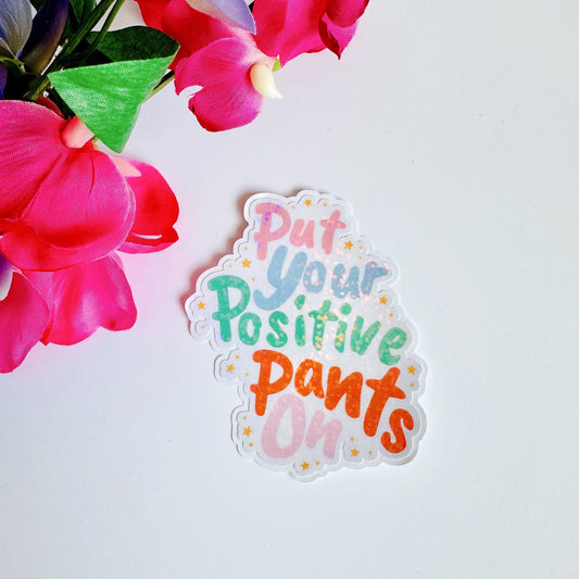 A holographic sticker, of the words put your positive pants on. The sticker has an easy peel lip.