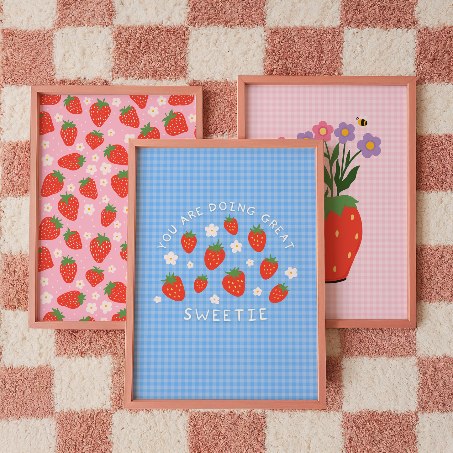 Three framed prints on a checkered wall with strawberry patterns and text.