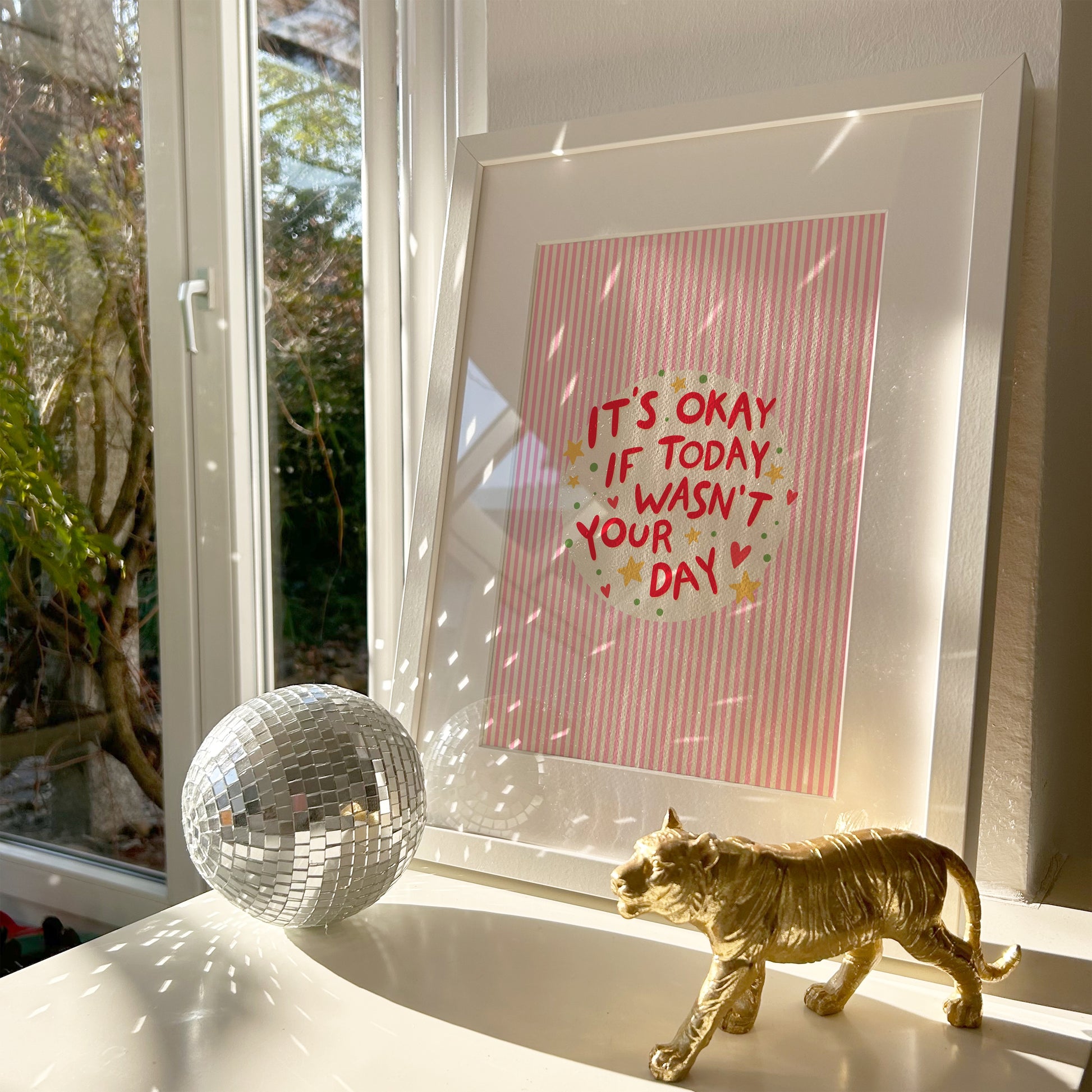 A red striped artwork, shown in a frame, with a motivational quote in the centre, decorated with stars and hearts.