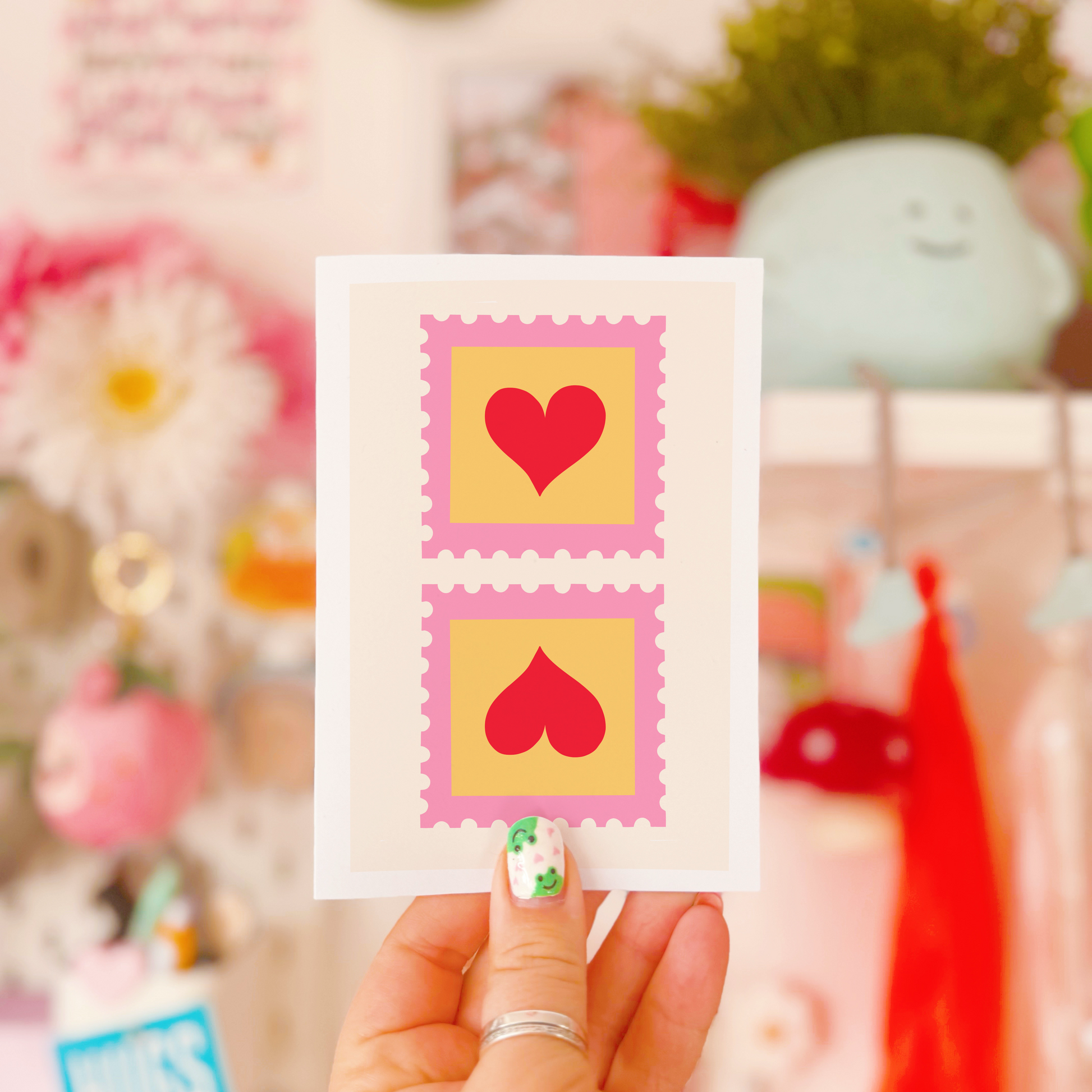 A greetings card with two illustrated postage stamps with red love hearts on.