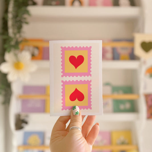 A greetings card with two illustrated postage stamps with red love hearts on.