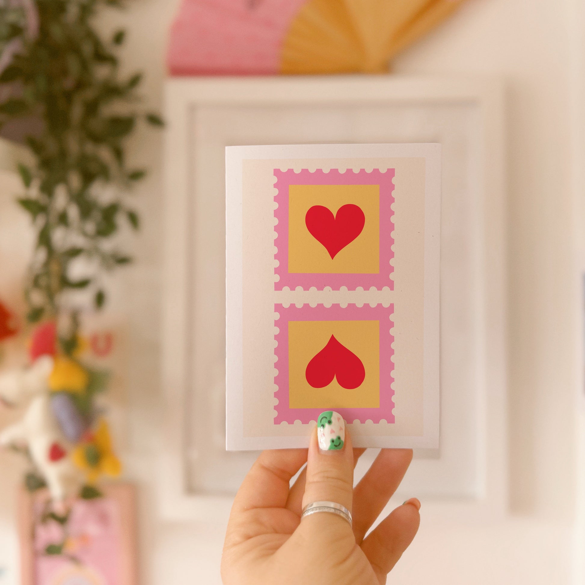 A greetings card with two illustrated postage stamps with red love hearts on.