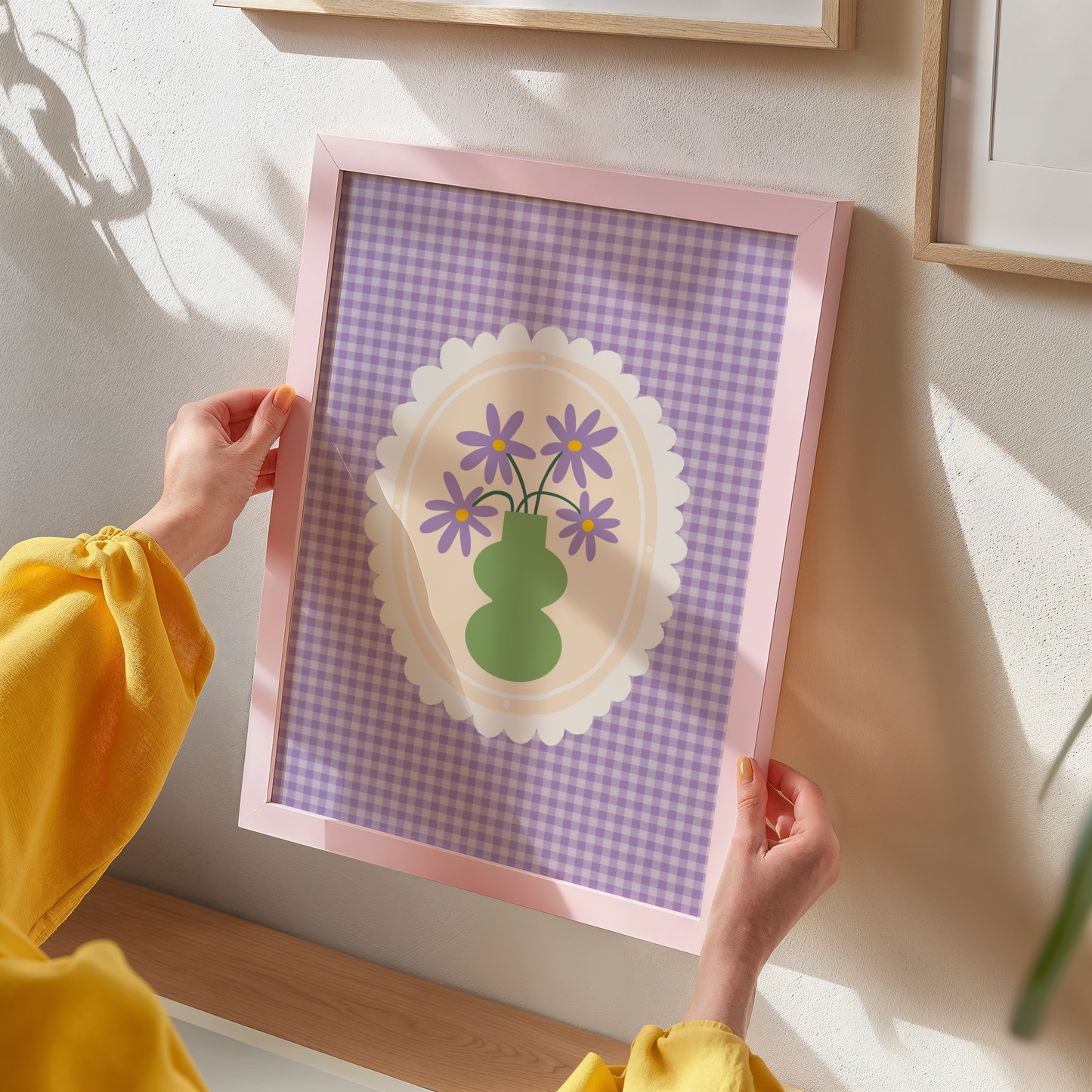 A purple gingham print, with a scalloped frame illustration in the centre. Inside the frame is an illustration of a green vase with purple daisies.