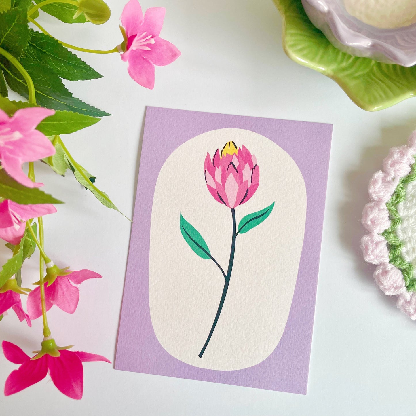 An illustration of a tulip stem, with a purple frame printed onto a textured postcard.