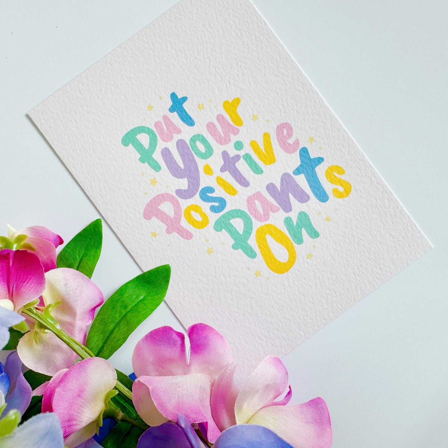 A textured postcard, with the words put your positive pants on, on the front, in pastel colours.