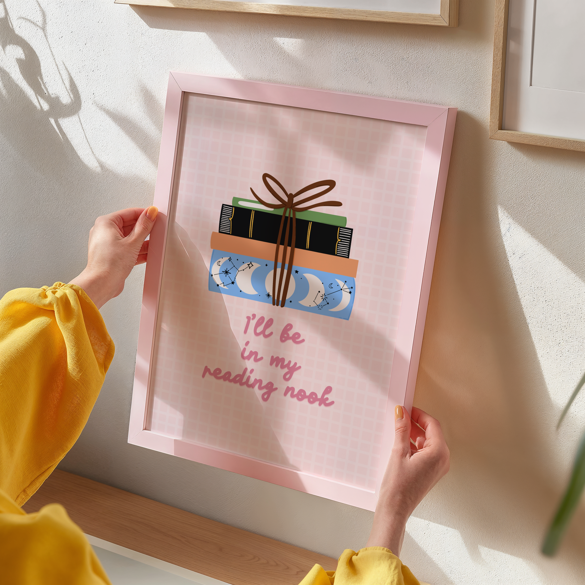 A cute pink print, featuring an illustration of a pack of books, and the quote 'I'll be in my reading nook' underneath.