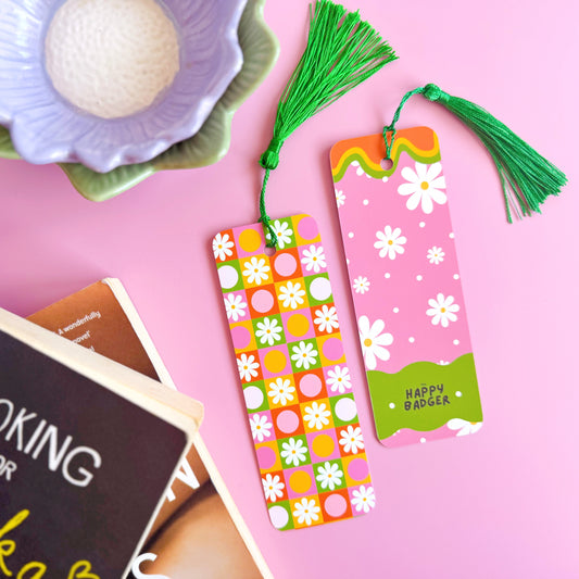 A brightly coloured retro look bookmark, featuring a checkerboard pattern with daisies and circles, in pink, green, yellow and orange. The bookmark has a coordinating green tassel.